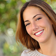 Young brunette woman wears a beige wool sweater and smiles at the camera