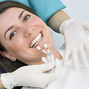 Woman smiles at the camera, while gloved hands hold dental instruments and wear a dental professional's uniform